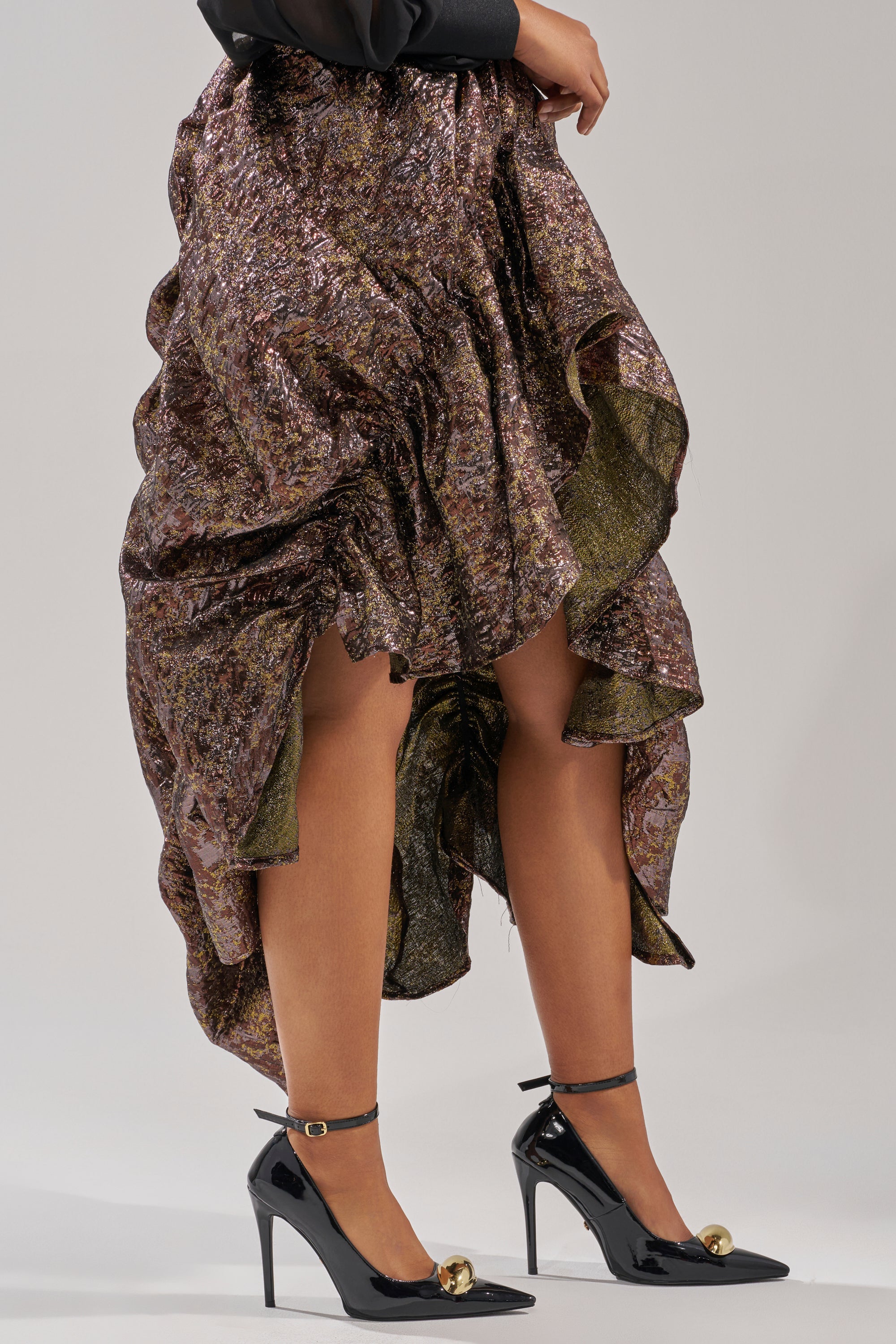 Wearing the CRAZY FOR YOU BROCADE RUCHED MIDI SKIRT and black ankle-strap heels with gold sphere accents, a person stands against a plain light background. 3