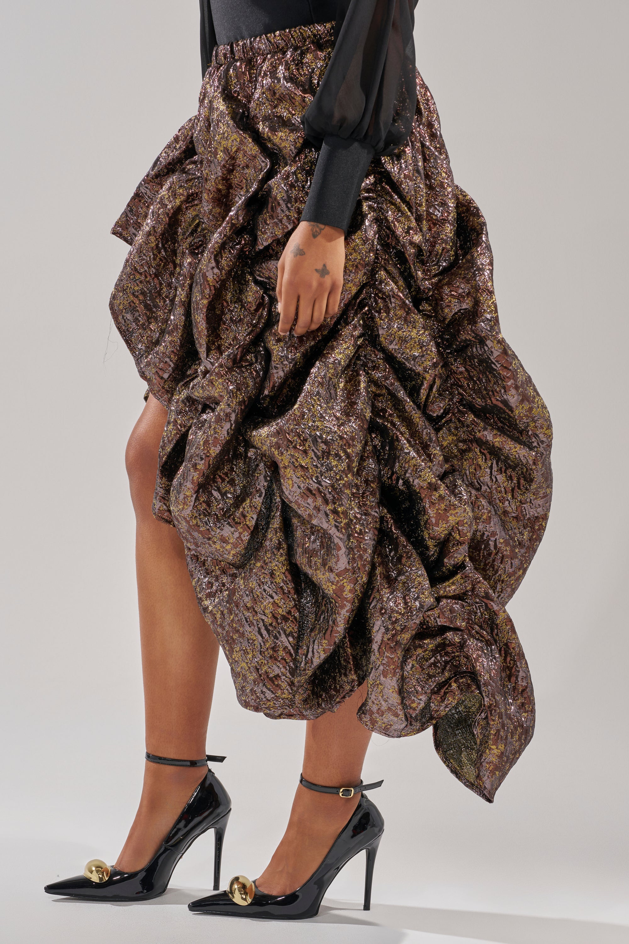 A person wearing the CRAZY FOR YOU BROCADE RUCHED MIDI SKIRT with black pointed-toe high heels featuring ankle straps and gold embellishments. Only the lower half of the body is visible. 4