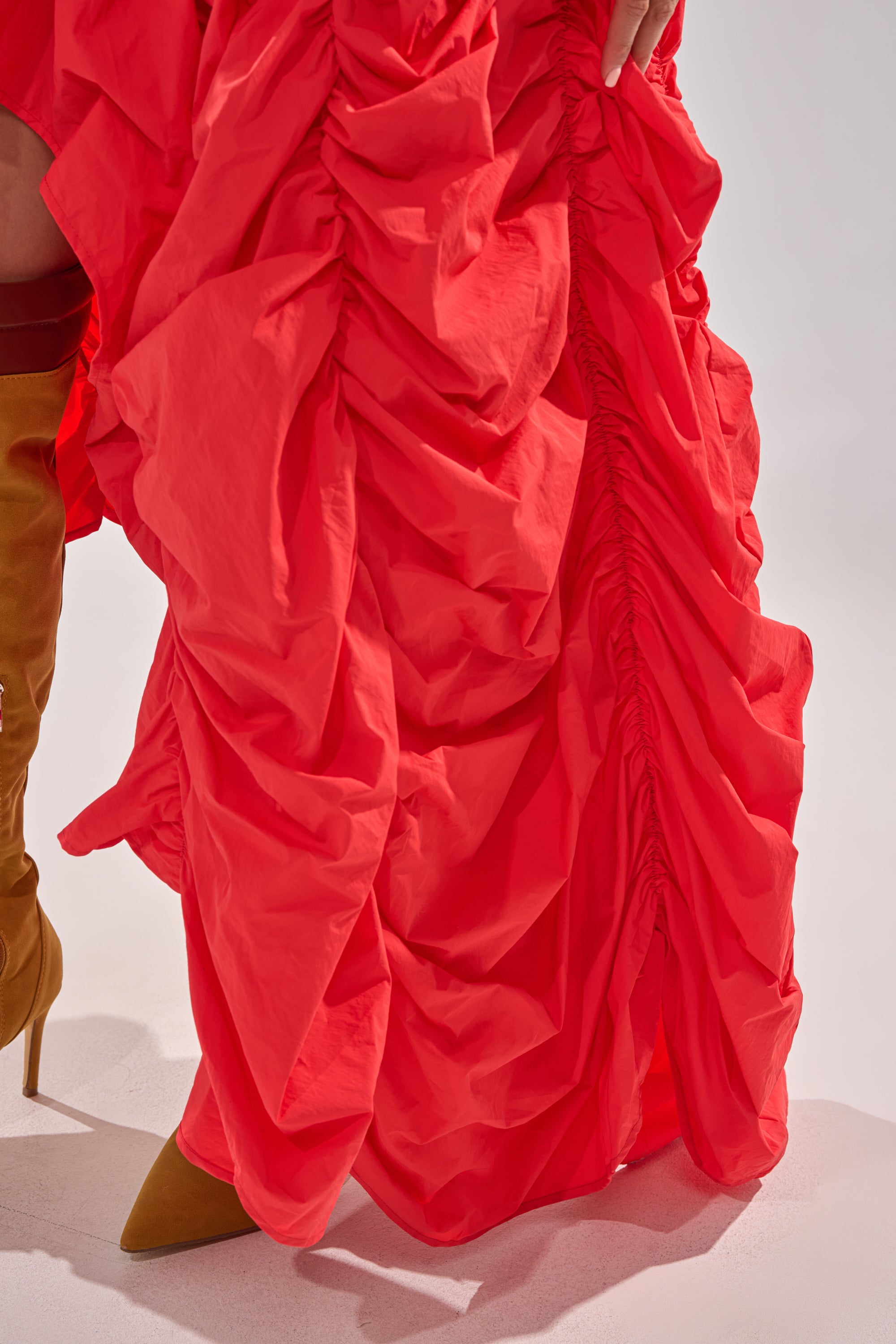 Wearing the LETS CHANGE IT UP RUCHED MIDI SKIRT IN RED, a person poses with one leg showing, styled with mustard yellow heeled boots against a plain background. 9