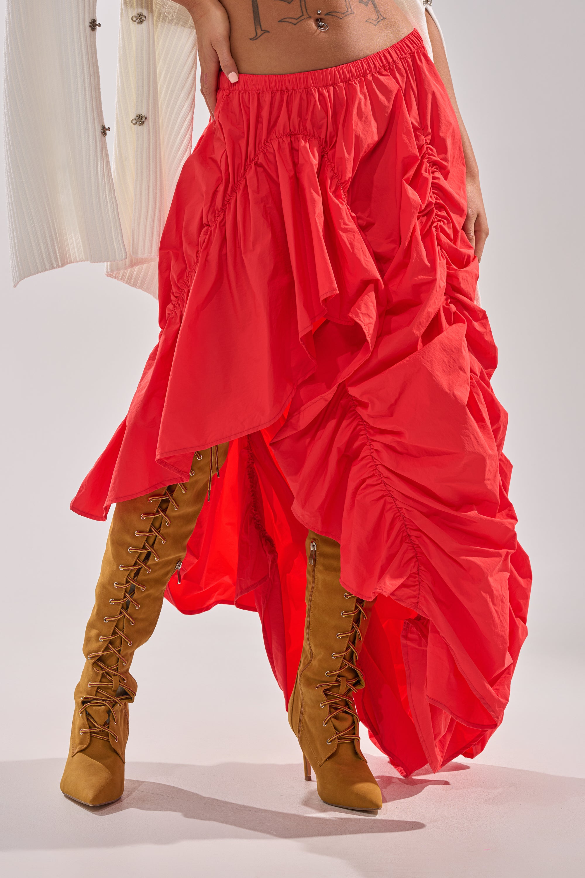 Wearing the LETS CHANGE IT UP RUCHED MIDI SKIRT IN RED, paired with tan lace-up boots and a crisp white button-up shirt, only the lower half of the person’s body is visible. 1