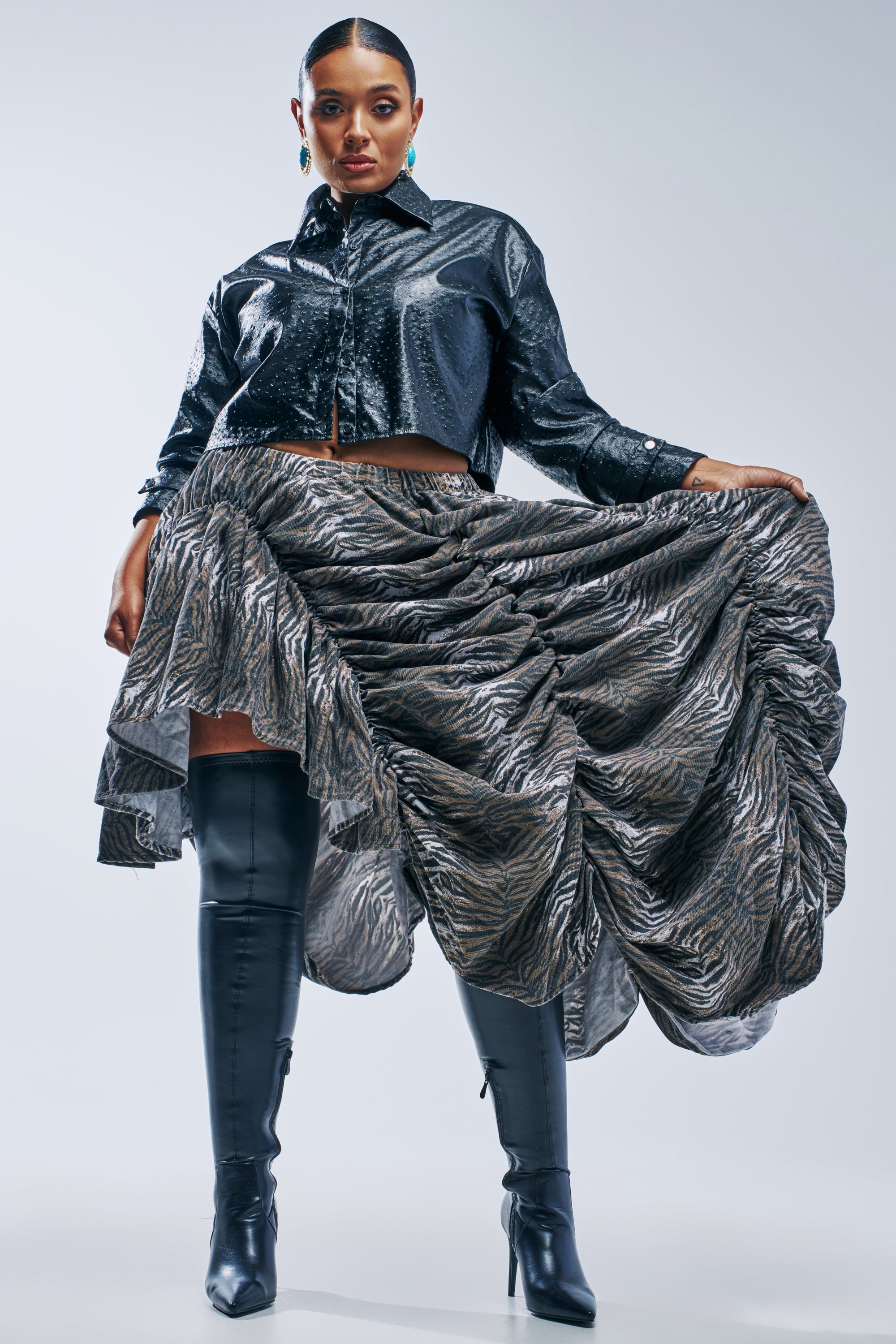 A person wearing a cropped black jacket and the ALL OVER THE PLACE RUCHED MIDI SKIRT in a grey and brown animal print, paired with black over-the-knee heeled boots.