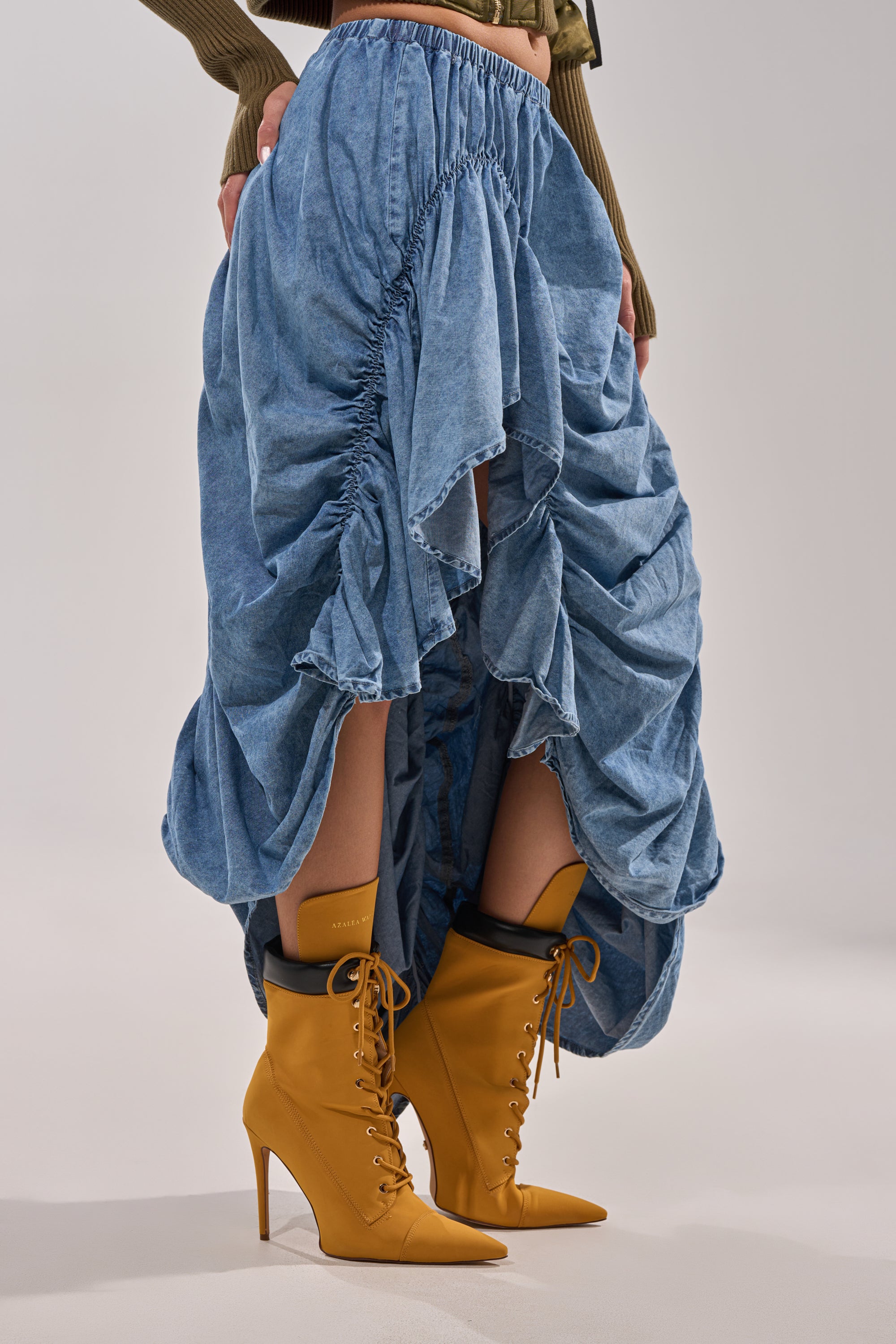 A person wears the LETS CHANGE IT UP RUCHED MIDI SKIRT IN CHAMBRAY, tan lace-up high-heeled ankle boots, and a partially visible olive green long-sleeve top. 4