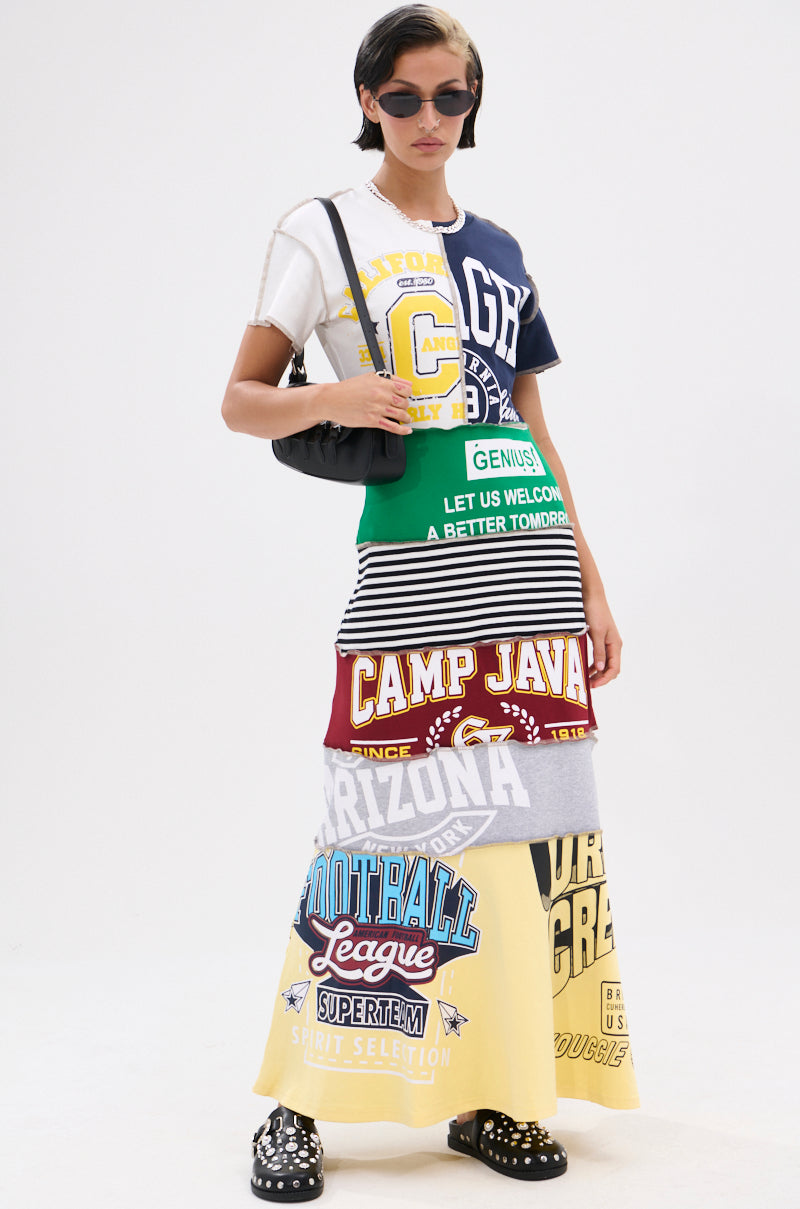 Radiating confidence, a person wears the COOL GIRL ENERGY TSHIRT MAXI DRESS with vibrant collegiate prints, paired with sunglasses and a black bag, posed against a plain white background.