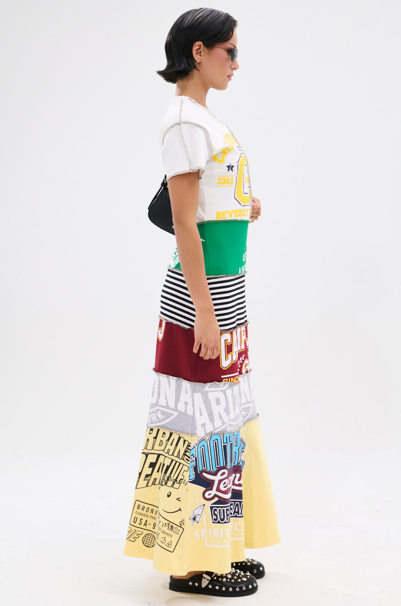 A woman with short dark hair exudes cool girl energy in sunglasses and the COOL GIRL ENERGY TSHIRT MAXI DRESS, styled with a black bag and studded shoes. She stands in profile against a white background.