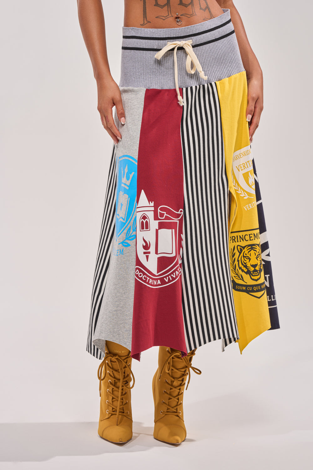 A person in the MIXED FEELINGS MIDI SKIRT—colorblock with crest details, stripes, and drawstring waist—paired with mustard yellow lace-up boots for a sporty streetwear look highlighting the lower torso and legs.