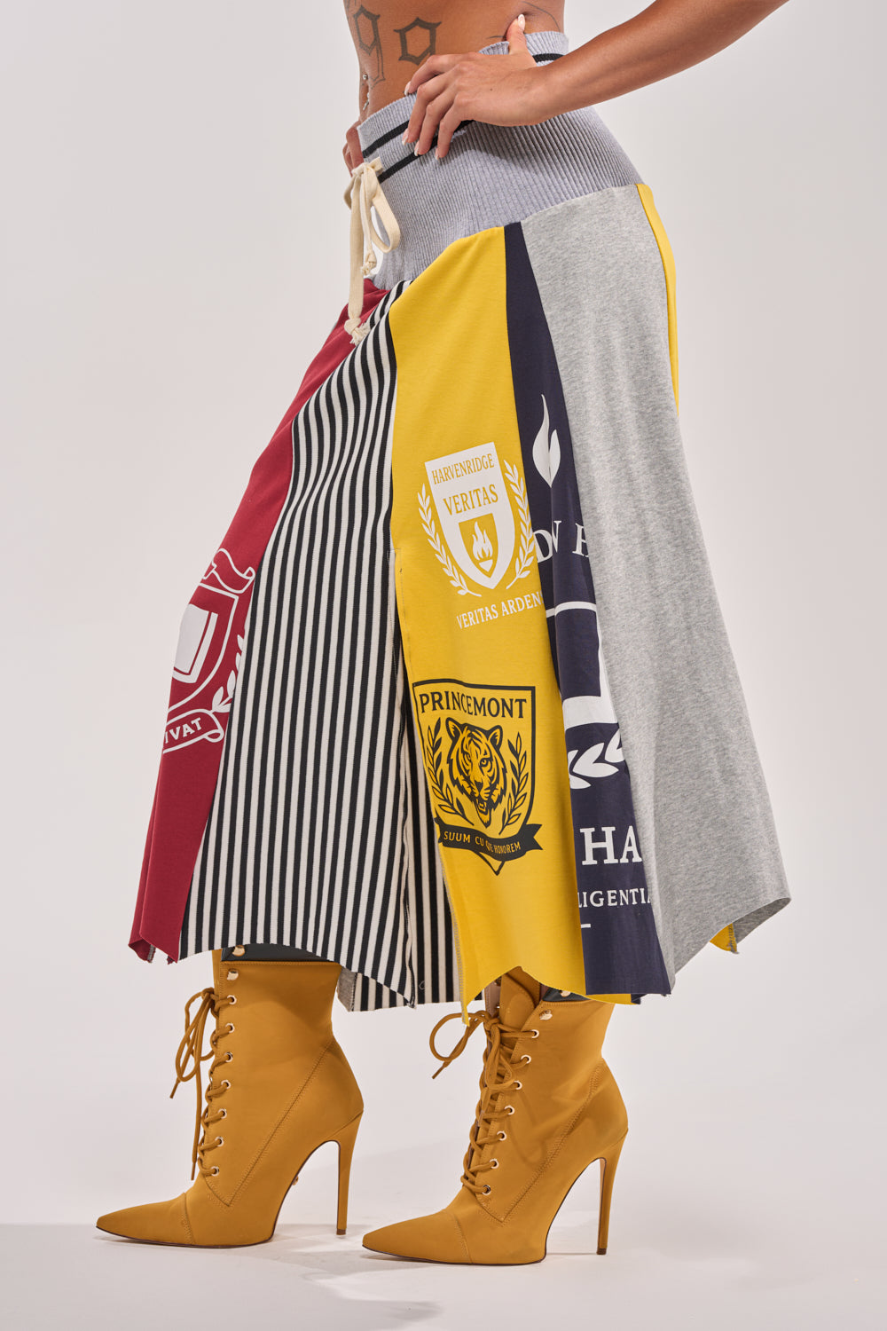 Sporty streetwear vibes: only the lower torso and legs are shown, featuring a MIXED FEELINGS MIDI SKIRT with crest designs and bold colorblocking, paired with mustard yellow lace-up heeled boots. 4