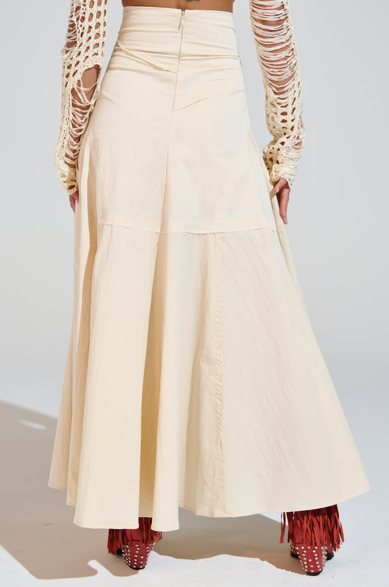 Someone is wearing the CLAIRE EXPOSED SEAMS MIDI SKIRT in cream, with an A-line silhouette and a textured long-sleeve top with intricate cutouts. Paired with red fringed boots, the back pose showcases the skirt's flow and design beautifully. 5