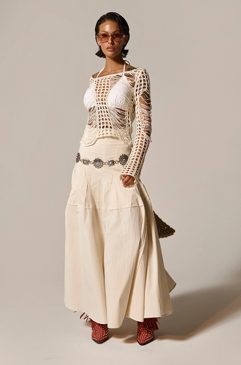 A person wears a white crochet top over a white bra, paired with the CLAIRE EXPOSED SEAMS MIDI SKIRT and an embellished belt. Red studded footwear peeks below. They have sunglasses and short hair, standing confidently against a plain background. 9