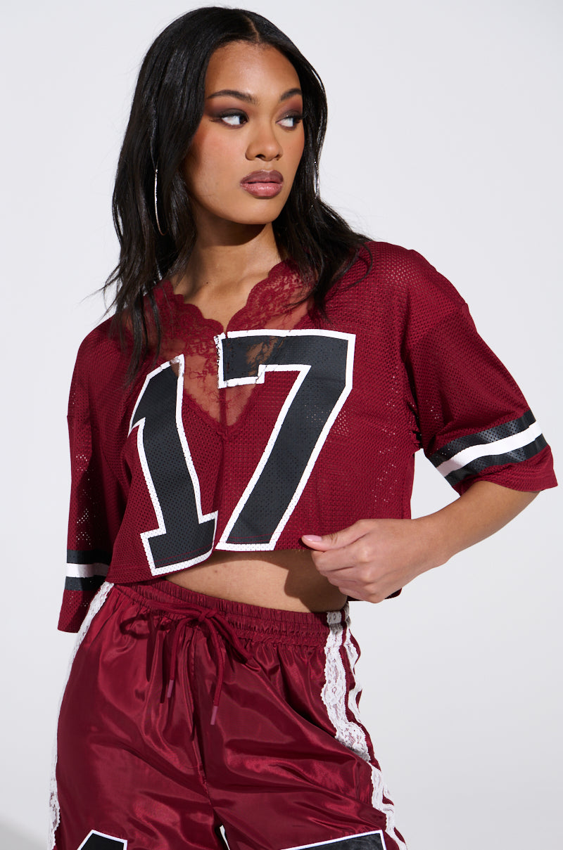 She wears the LETS GET IT JERSEY, a sporty red mesh top with the number 17, paired with matching shorts. Hoop earrings enhance her look as she flaunts her long dark hair while glancing to the side.