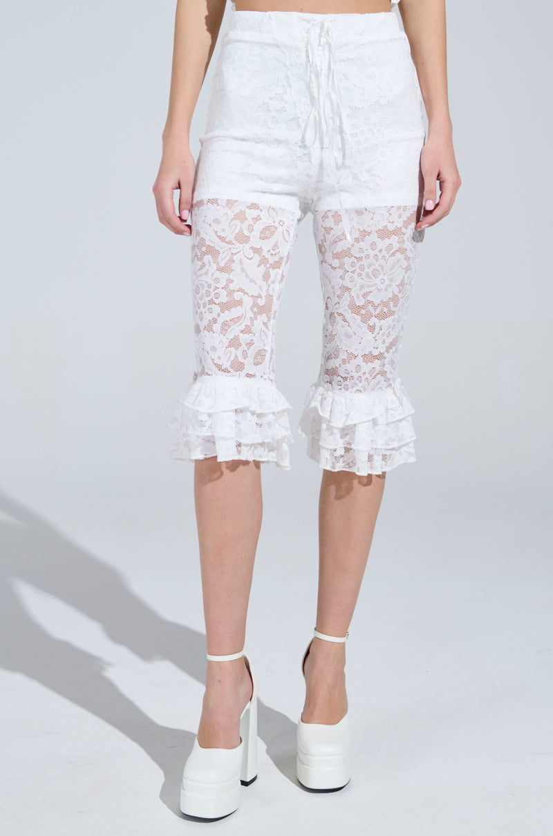 Someone is wearing GIRLY POP LACE CAPRI LEGGINGS with ruffled hems, paired with platform white heels against a plain light background. 1