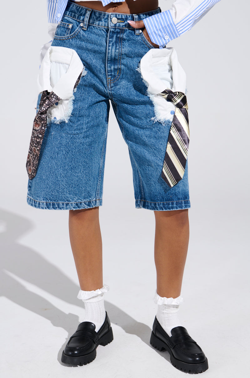 Wearing knee-length STANDING ON BUSINESS BERMUDA SHORT with frayed white pockets and attached ties, paired with white socks, black loafers, and a blue and white striped shirt against a gray backdrop creates a casual yet refined look that expertly blends laid-back style with high-rise fit elegance.