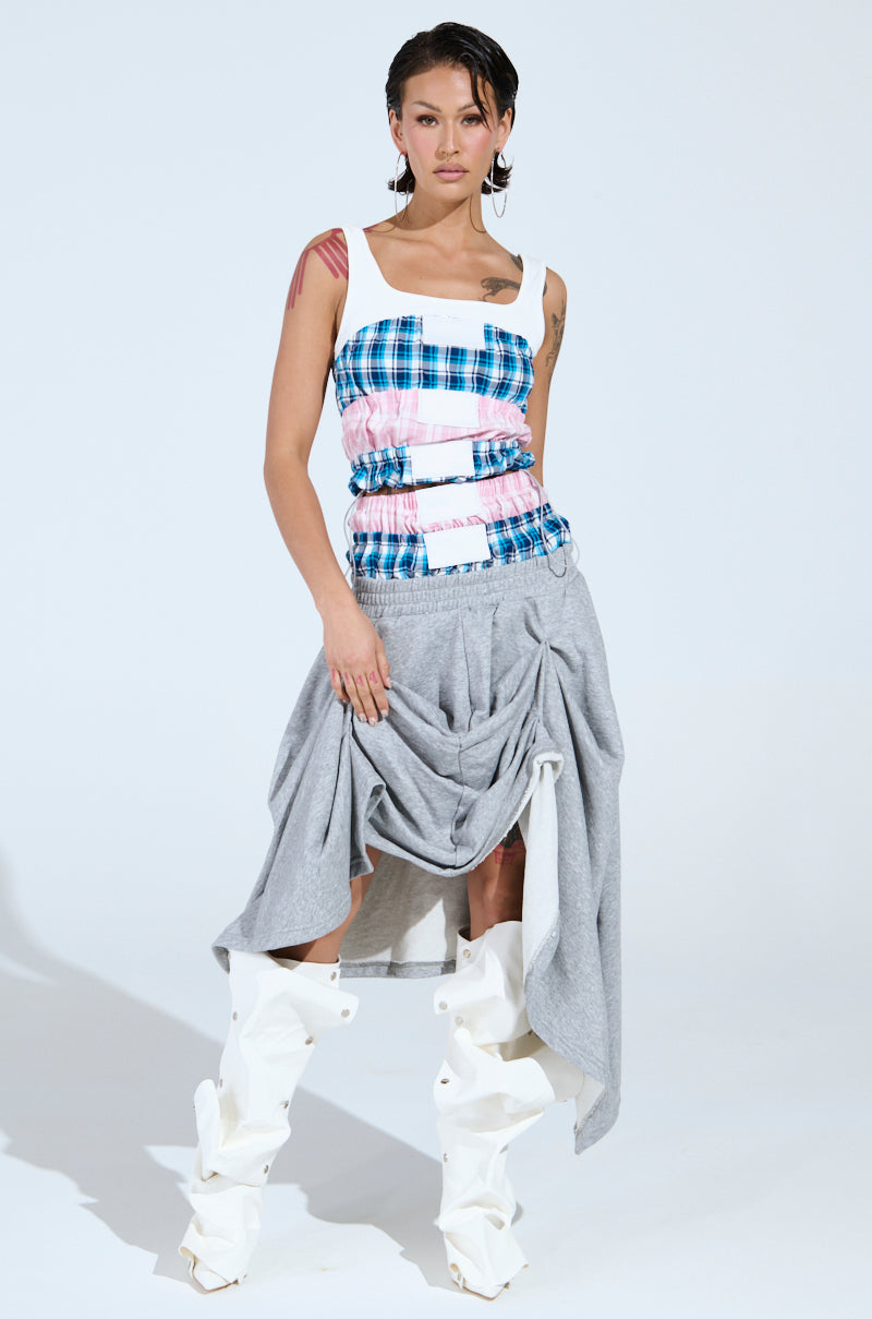 A person with short dark hair and visible tattoos stands against a light background wearing the DONT MESS WITH ME TANK, featuring a blue, pink, and white plaid design, styled with a draped gray skirt and white slouchy knee-high boots.