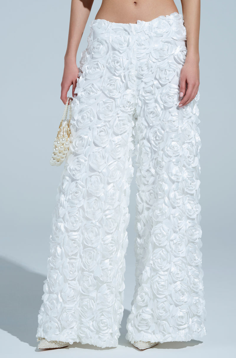 Someone is wearing ROSE PETAL WIDE LEG PANT with elegant rose appliques, paired with a small pearl handbag against a simple, light blue background.