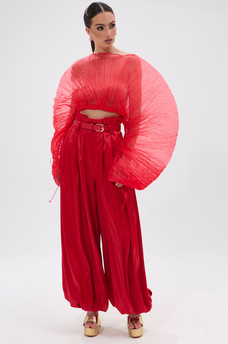 A woman poses in a studio wearing the bold FORTUNE'S FAVORITE ORGANZA CROP TOP IN RED with dramatic fan-like sleeves, matching high-waisted wide-leg pants, and metallic gold platform shoes—a standout Fortune’s Favorite look.