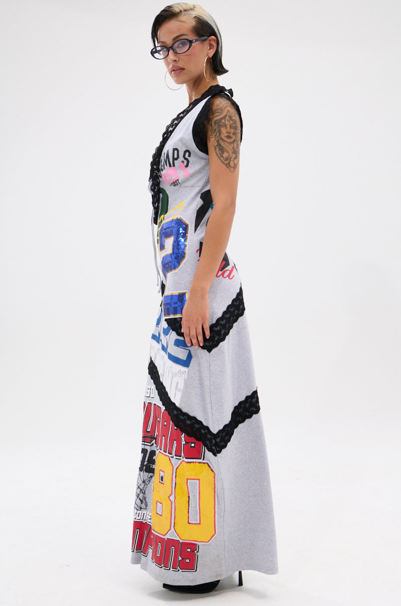 A woman with glasses and tattoos models the INSTA SAW IT FIRST GRAPHIC MAXI DRESS, a sporty bodycon maxi with number graphics and black braided details, standing against a plain white background.