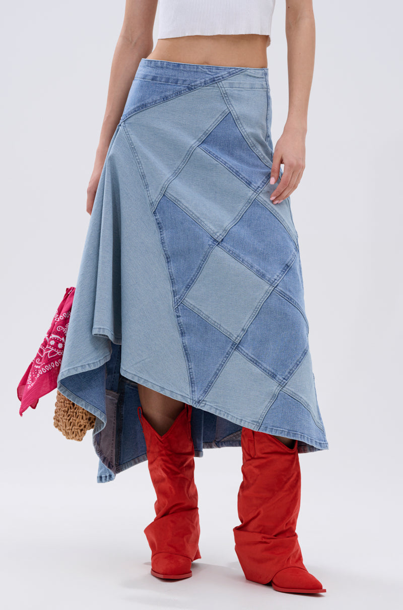 Someone wears the ALL WE NEED IS LOVE DENIM MIDI SKIRT with a white crop top and bright red suede boots. A pink bandana and textured bag peek out from beneath the skirt against a simple, light background.