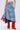 Someone wears the ALL WE NEED IS LOVE DENIM MIDI SKIRT with a white crop top and bright red suede boots. A pink bandana and textured bag peek out from beneath the skirt against a simple, light background.