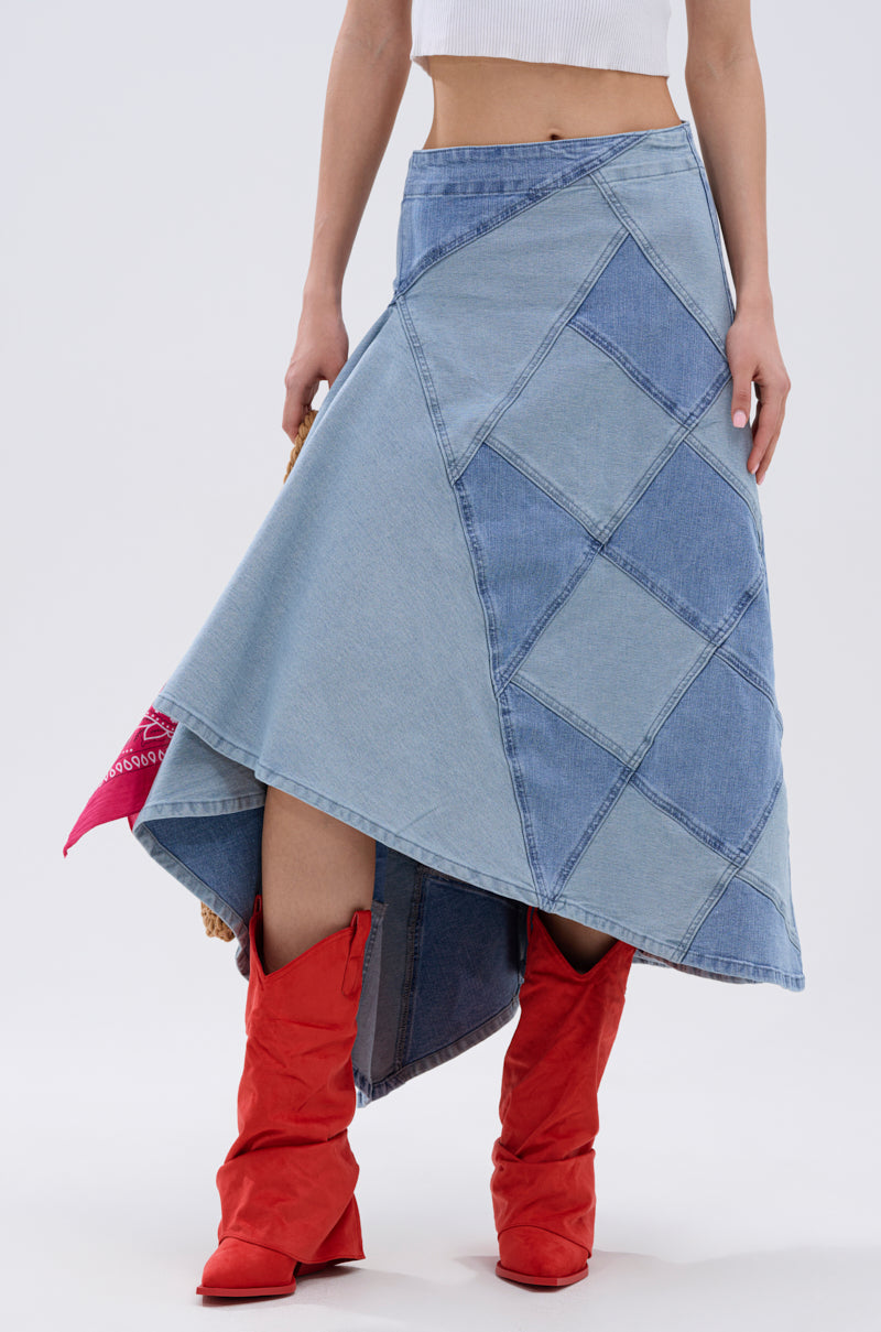 A person stands against a plain light background, showing only the lower torso and legs, styled in a white crop top, bright red boots, and the ALL WE NEED IS LOVE DENIM MIDI SKIRT.