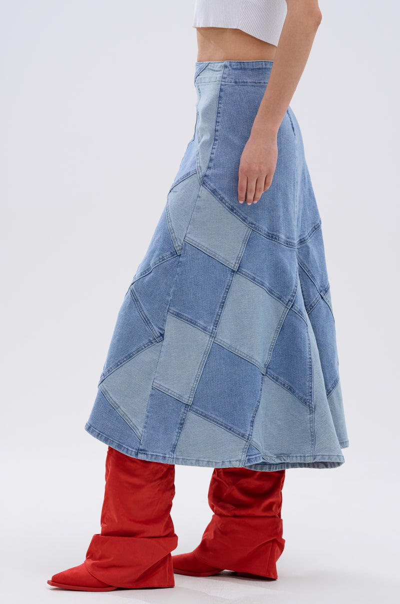 A person is shown from the side against a plain, light background wearing the ALL WE NEED IS LOVE DENIM MIDI SKIRT, a white sleeveless crop top, and bright red slouchy knee-high boots.