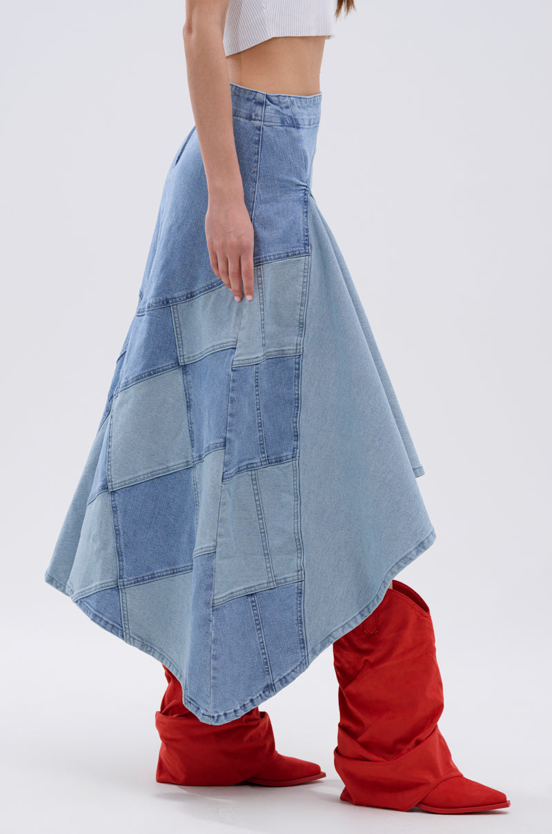 A woman stands sideways against a plain background wearing a white crop top, tall red boots, and the ALL WE NEED IS LOVE DENIM MIDI SKIRT with a patchwork design and asymmetric hem.