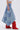 A woman stands sideways against a plain background wearing a white crop top, tall red boots, and the ALL WE NEED IS LOVE DENIM MIDI SKIRT with a patchwork design and asymmetric hem.