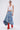 A woman in sunglasses, hoop earrings, a white crop top, and red knee-high boots confidently poses against a light background wearing the ALL WE NEED IS LOVE DENIM MIDI SKIRT.