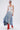 A woman in sunglasses and hoop earrings models the ALL WE NEED IS LOVE DENIM MIDI SKIRT—a high-rise patchwork denim midi—paired with a white fringe crop top and red boots against a plain background.