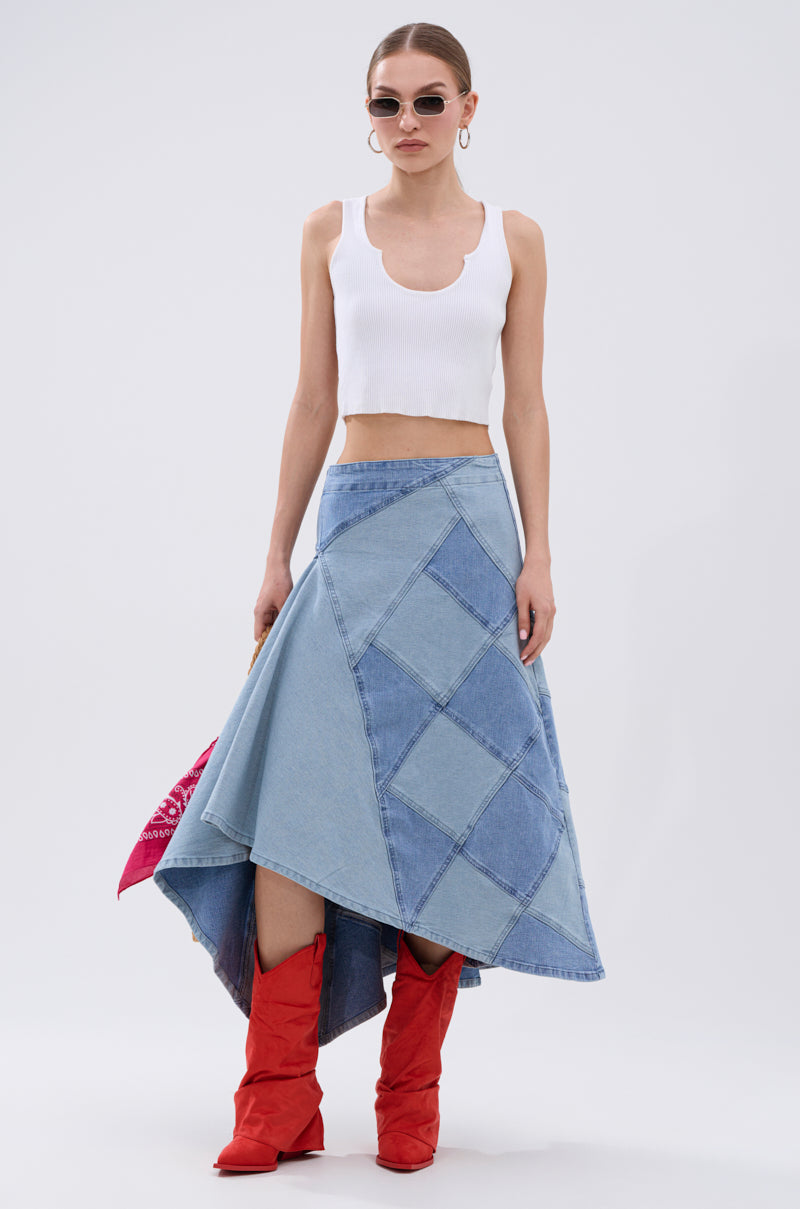 A woman stands against a plain background wearing sunglasses, a white crop top, red knee-high boots, and the ALL WE NEED IS LOVE DENIM MIDI SKIRT, holding a red bandana.