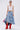 A woman stands against a plain background wearing sunglasses, a white crop top, red knee-high boots, and the ALL WE NEED IS LOVE DENIM MIDI SKIRT, holding a red bandana.