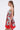 Woman with long straight brown hair wears the ON VACAY PRINTED SATIN MINI DRESS, featuring a strapless sweetheart neckline, red and green rose pattern, and handkerchief hem, standing in profile against a plain light background.