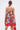 A woman with straight brown hair in a low ponytail models the ON VACAY PRINTED SATIN MINI DRESS, featuring a strapless sweetheart neckline, red and green rose print, handkerchief hem, and holds a red handbag. She is shown from the back against a light background.
