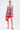 A woman wears the ON VACAY PRINTED SATIN MINI DRESS, a strapless sweetheart mini with red and white floral print and handkerchief hem, styled with a matching red handbag and red strappy heels against a white background.