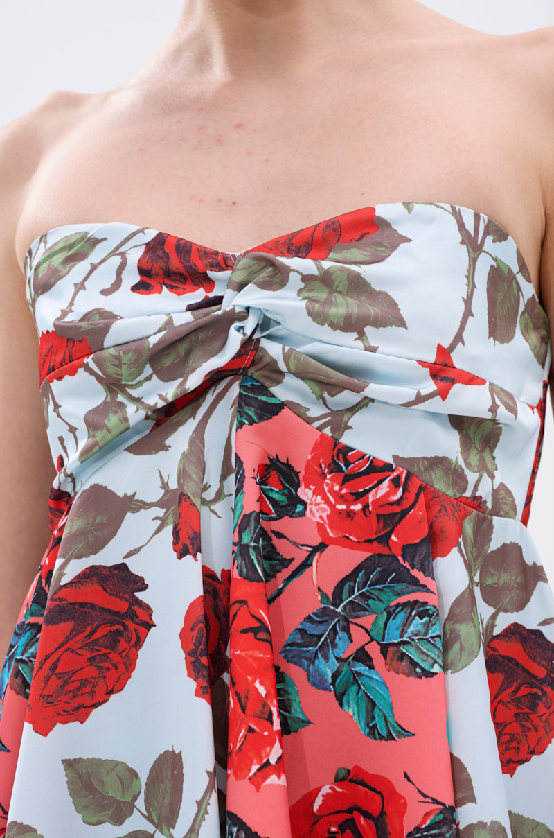 The ON VACAY PRINTED SATIN MINI DRESS showcases a strapless sweetheart neckline with a twisted bust knot and bold red and green rose print on light blue and coral satin, highlighting the shoulders and upper chest.
