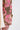 A close-up shows a hand and arm wearing the LIGHT THE WAY BROCADE BLAZER in pink floral brocade, its intricate sleeve contrasting with adjacent light cream fabric on a green and brown background.