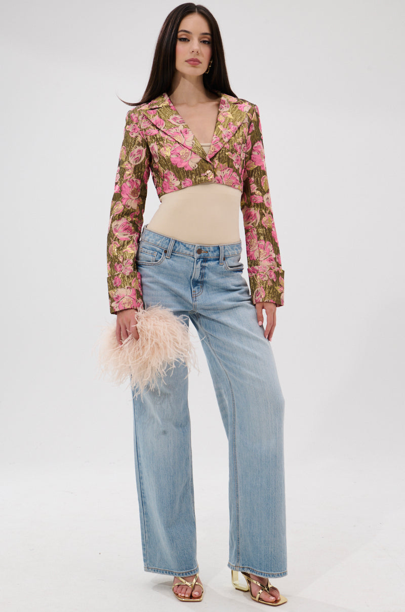 A woman stands against a white background wearing the LIGHT THE WAY BROCADE BLAZER, a beige top, light blue wide-leg jeans, gold heeled sandals, and holding a feathery pale pink clutch. 7