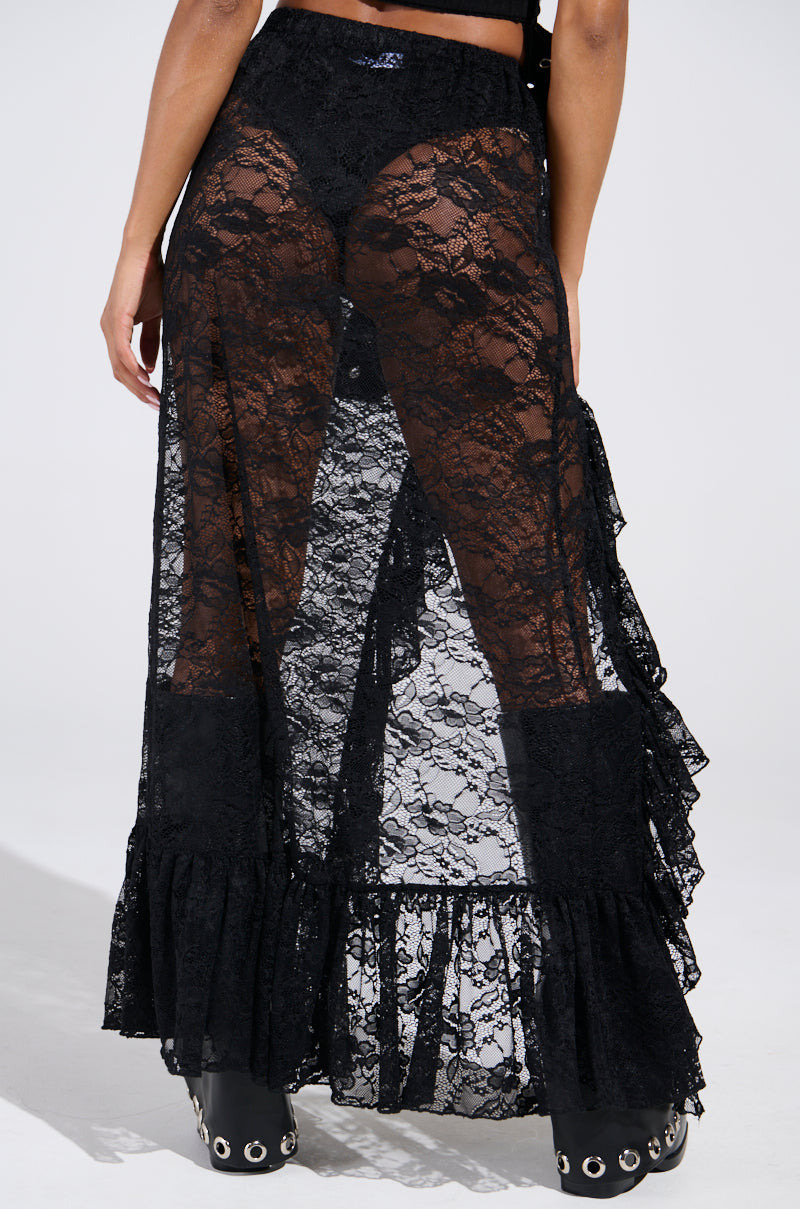 A person flaunts a festival-ready look by layering the "DANCE THE NIGHT AWAY LACE MAXI SKIRT," featuring sheer black lace ruffles and an intricate floral pattern over solid fabric, paired elegantly with matching black footwear against a plain white backdrop.