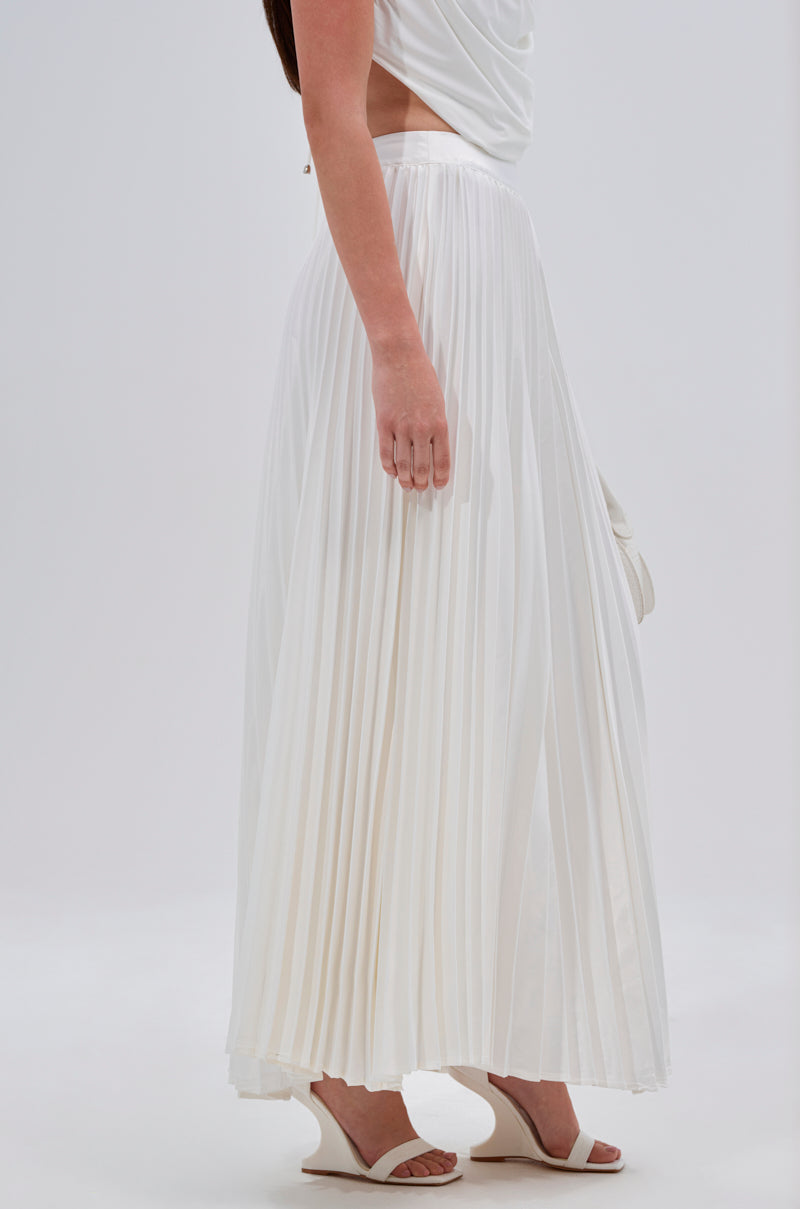 A person models the SWEET THING PLEATED SATIN MAXI SKIRT—a white, high-rise, pleated A-line maxi—paired with a sleeveless white top and sandals, standing against a plain light background. 2