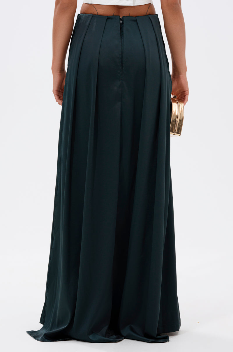 A person is shown from the back wearing the LOOK AT ME GO TROUSER WITH TAIL in dark green and holding a small gold clutch, standing against a plain white background.