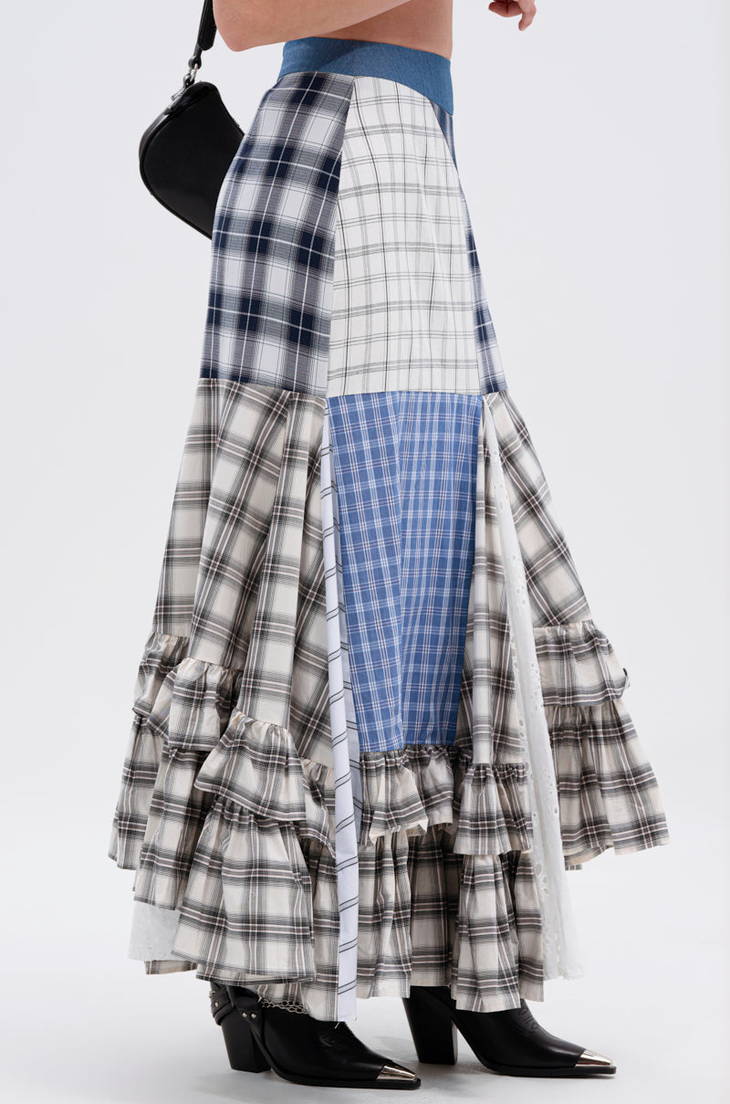 A person wears the OUT OF ALIGNMENT PLAID MIDI SKIRT with a denim high-rise waistband, styled with pointed black boots and a black crossbody bag, shown from the side against a plain background.