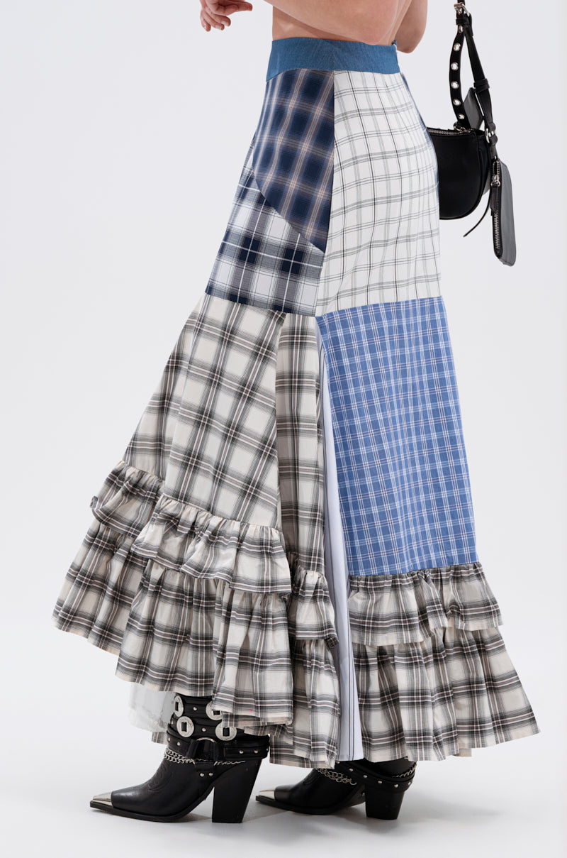 Wearing the OUT OF ALIGNMENT PLAID MIDI SKIRT with a denim high-rise waistband, ruffles, and side slit, styled with black studded boots and a black handbag for a bold mix of blue, white, and gray patterns.