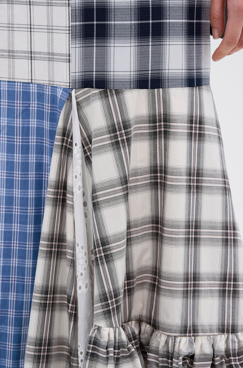 A close-up of a person holding the OUT OF ALIGNMENT PLAID MIDI SKIRT, featuring blue, black, and white plaid fabrics with gathered ruffles and white eyelet lace details.