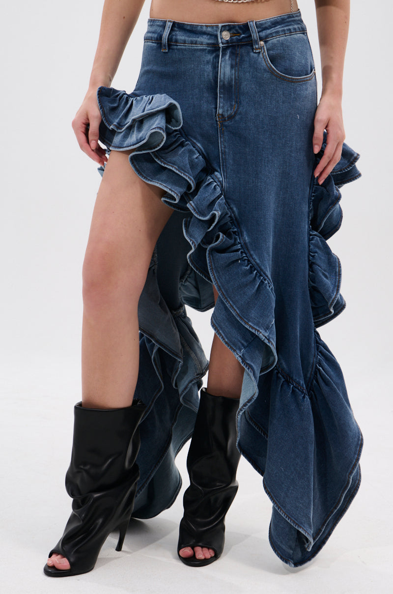 A person wears the DONT MESS WITH MY HEART DENIM RUFFLE SKIRT, featuring a high waist, ruffles, asymmetrical hem, and high slit, styled with black slouchy open-toe boots against a plain white background.