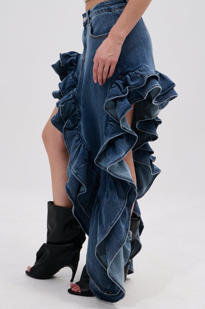 Wearing the DONT MESS WITH MY HEART DENIM RUFFLE SKIRT with dramatic ruffled side slits and black open-toe heeled boots, a person poses against a plain light background.