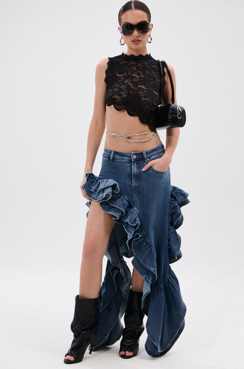 A person in a black lace crop top, the DONT MESS WITH MY HEART DENIM RUFFLE SKIRT with a high slit, black open-toe boots, sunglasses, a small black shoulder bag, and a chain belt stands against a plain white background.