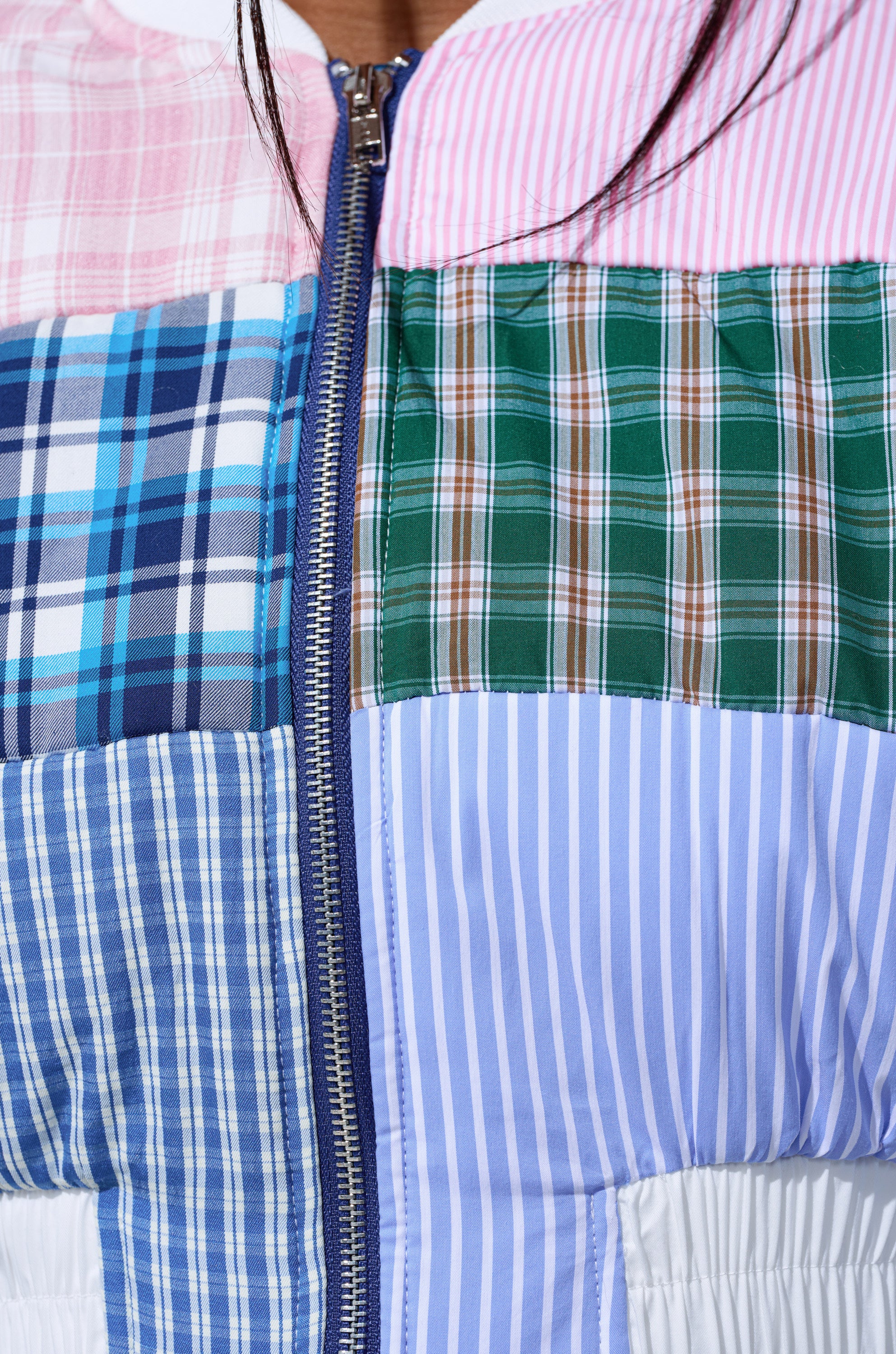 Close-up of the BABY GIRL PATCHWORK BOMBER, a cropped jacket crafted from mixed plaid and striped fabrics in pink, green, blue, and white, with a visible silver zipper at the center.