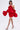 A woman models the CHIC AF RUFFLE MINI DRESS IN RED, featuring dramatic ruffled sleeves and a rose accent on the bodice, with a fitted mini skirt and black strappy high heels against a plain backdrop.