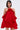 A woman with straight, shoulder-length dark hair models the CHIC AF RUFFLE MINI DRESS IN RED, featuring an off-the-shoulder rose-accented neckline, flowing sleeves, and a satin-textured skirt. She stands against a plain background.