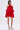 A woman faces forward in a red CHIC AF RUFFLE MINI DRESS with floral details and flowy satin fabric. She has straight dark hair, hoop earrings, and strappy black high-heeled sandals. The background is plain white.