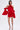 A woman wearing the CHIC AF RUFFLE MINI DRESS IN RED with a satin finish and black strappy heels stands against a plain white background.