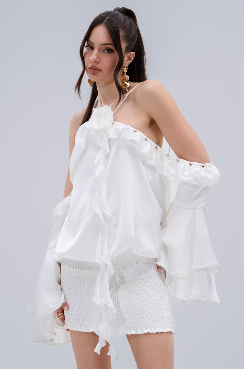 A woman poses against a plain light gray background wearing the CHIC AF RUFFLE MINI DRESS IN WHITE.